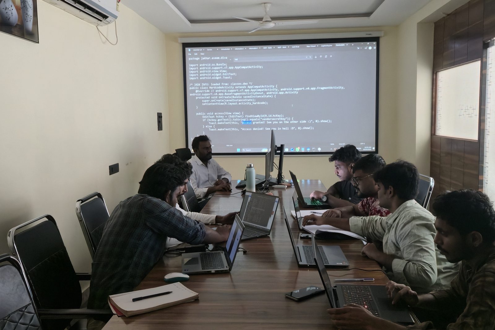Students at laptops around a long table in the Ameerpet training room, with a lesson on the projector screen